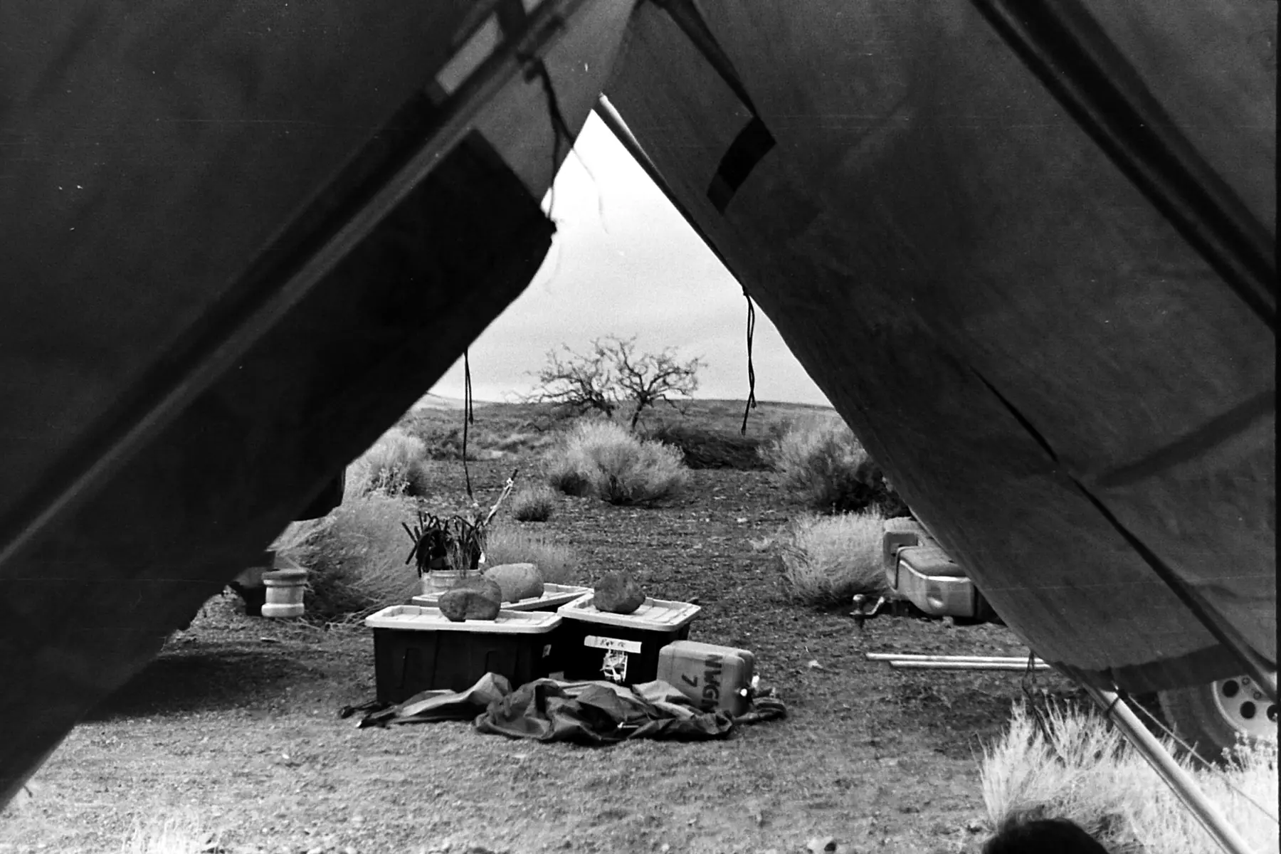 View across the Black Rock Desert through the opening of a temporary camp shelter, with packed bins and equipment in the foreground.